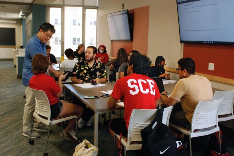 Instructor Oh Moon Kwon, left, speaks to students during a math class, part of an intense six-week summer bridge program for students of color and first-generation students at the University of Wisconsin, in Madison, Wis., July 27, 2022. Seated, in the flowered black shirt is Angel Hope, who said he didn't feel ready for college after online classes in high school caused him fall behind, but says the bridge classes made him feel more confident. Hundreds of thousands of recent graduates are heading to college this fall after spending more than half their high school careers dealing with the upheaval of a pandemic. (AP Photo)
