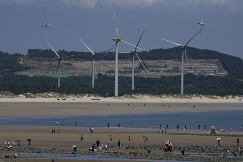 Beachgoers walk near wind turbines along the coast of Pingtan in Southern China's Fujian province, on Aug. 6, 2022. The world's two biggest emitters of greenhouse gases are sparring on Twitter over climate policy, with China asking if the U.S. can deliver on the landmark climate legislation signed into law by President Joe Biden this week. (AP Photo)