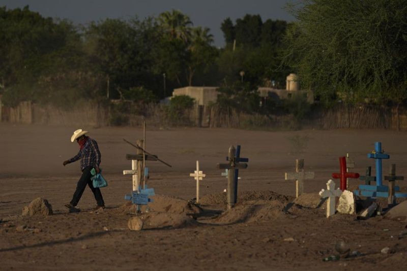 A Yaqui Indigenous wears a bandana over his mouth as he walks through dust past the cemetery where slain water-defense leader Tomás Rojo is buried in Potam, Mexico on September 27, 2022. Rojo was a descendent of Tetabiate, a Yaqui leader killed in a 1901 battle with the government, which deported the surviving Yaquis to work in slave-like conditions on henequen plantations in far-away Yucatan. (AP Photo)