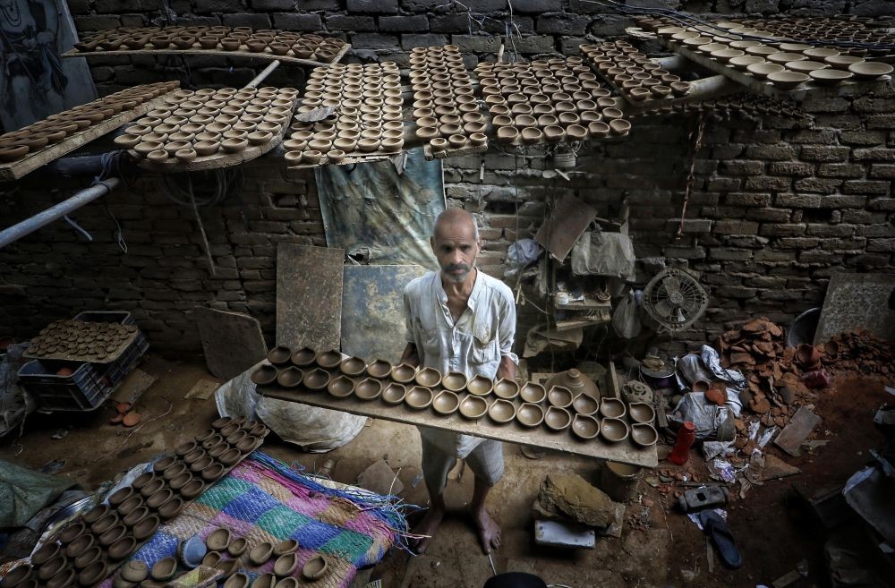 Delhi:A worker carries earthen lamps to dry before putting them into a furnace, in preparation for the upcoming Diwali festival,in New Delhi on Monday October 17, 2022(Photo: Wasim Sarvar/IANS)