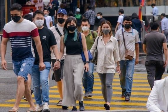 People wearing face masks walk across a street in Kuala Lumpur, Malaysia, Feb. 24, 2022. (Photo by Chong Voon Chung/Xinhua/IANS)