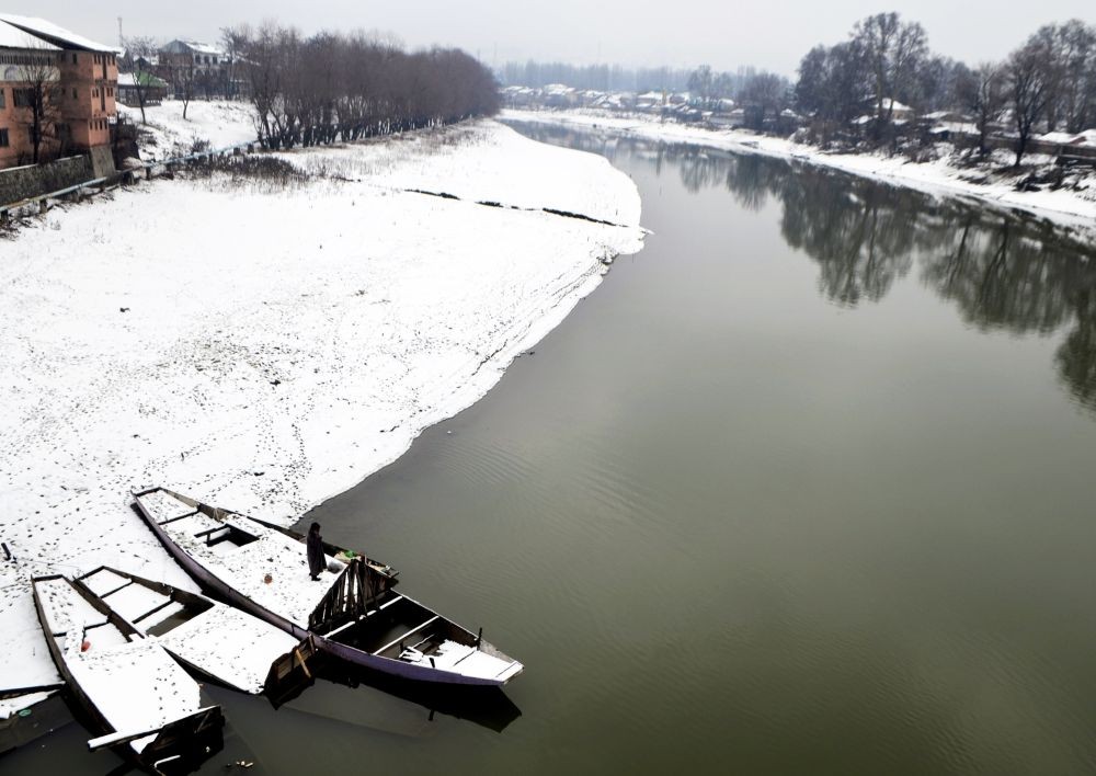 Boats anchored along the bank of Jhelum river as the area covered in a thick blanket of snow after heavy snowfall in Baramulla district on December 30, 2022. (IANS Photo)