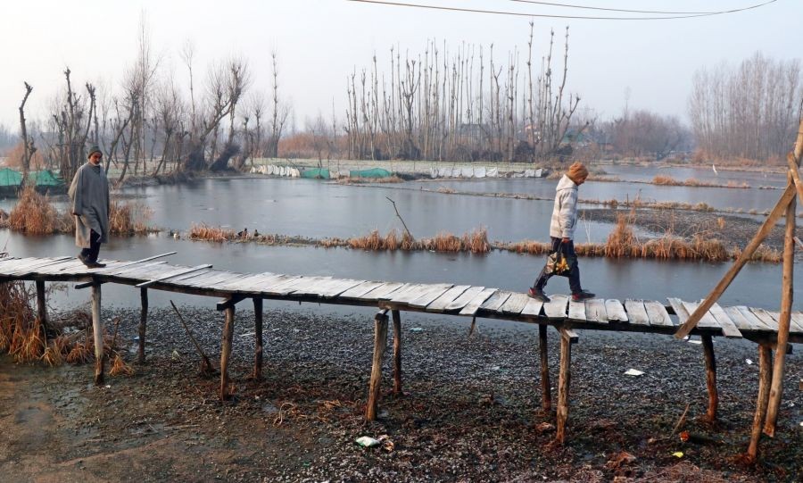 Srinagar: Two men walk over a footbridge to cross a frozen Dal Lake during a winter day, in Srinagar on Tuesday, Jan. 03, 2023. (Photo: Nisar Malik /IANS)