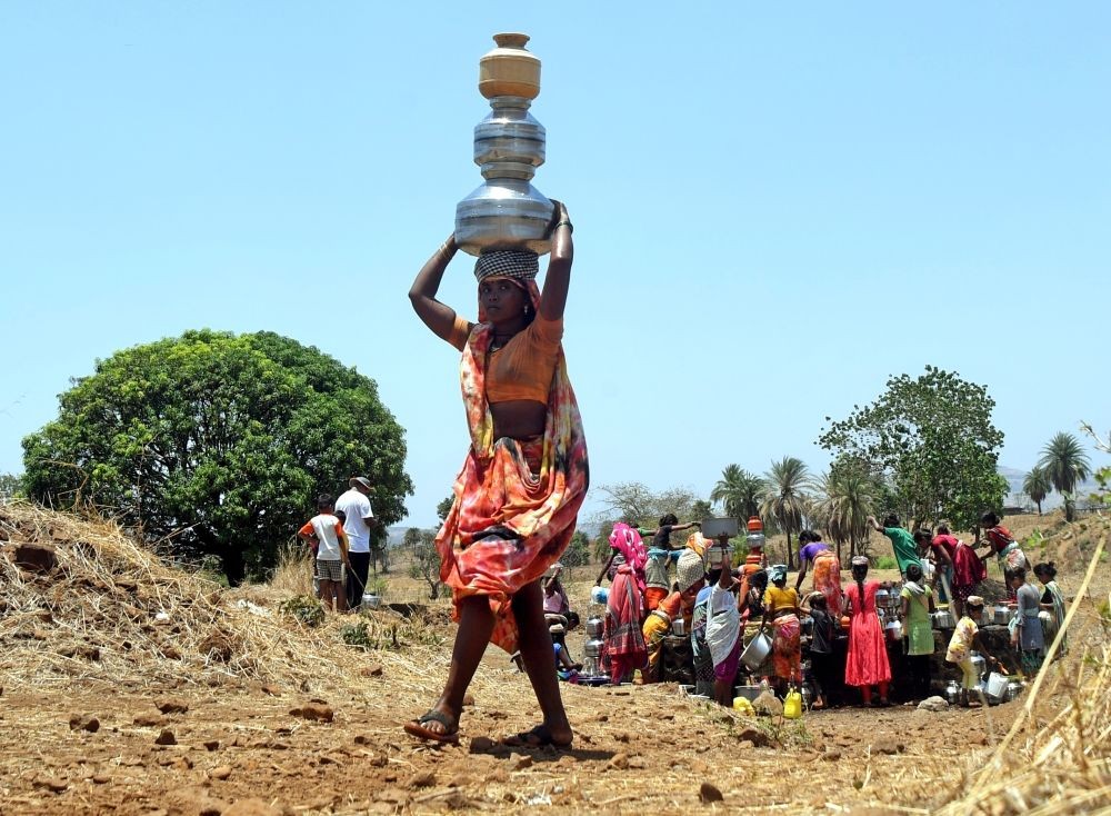 Thane : A woman departs with pots filled with water from a well, as villagers gather around a dry well to collect water provided by tankers in Shahapur Taluka, Thane District, Maharashtra on Sunday, May 14, 2023. (Photo:IANS)