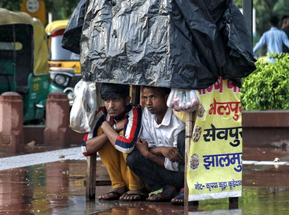 New Delhi: Street vendors take cover underneath their stall to protect themselves from rain, in New Delhi, on Wednesday, July 05, 2023. (Photo: IANS/Wasim sarvar)