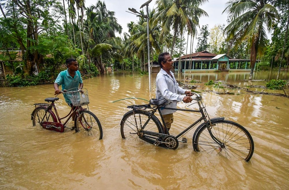 Nagaon: People push their cycles through floodwater following the landfall of Cyclone 'Remal' at Kampur in Nagaon on Thursday, May 30, 2024. (Photo: IANS/Anuwar Hazarika)