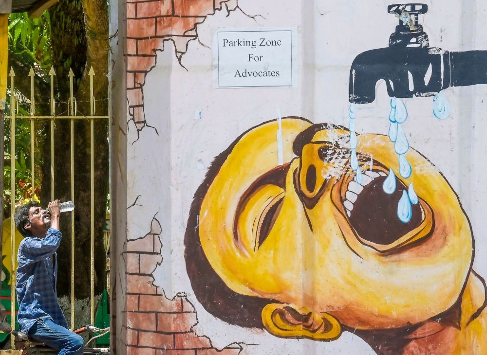 Agartala: A rickshaw puller drinks water near a wall adorned with graffiti to beat the heat on a hot summer day, in Agartala, Sunday, May 26, 2024.(IANS/Abhisek Saha)