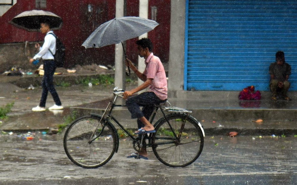 Nagaon: A man on a cycle holding umbrella crosses a road as it rains after the landfall of the Cyclone Remal, in Nagaon district of Assam, May 28, 2024.(IANS/Anuwar Hazarika)