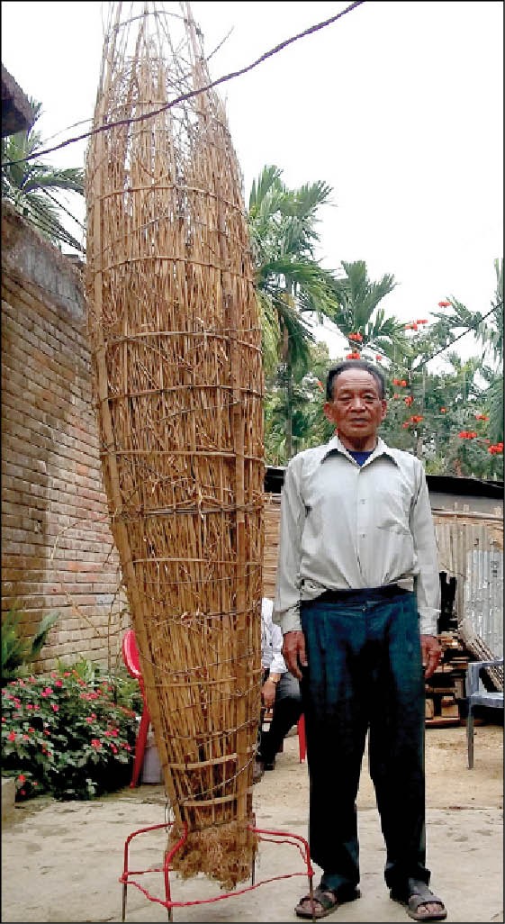 Melhite Kenye standing alongside a preserved and dried giant rice plant, an offspring of the “tallest paddy plant in the world” he discovered in 1998. The rice plant measures 9 feet.