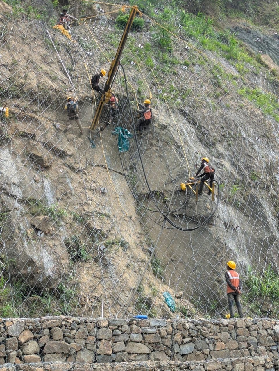 Workers are seen installing iron mesh along a vulnerable stretch of National Highway 29, just past the Chümoukedima check gate near the Patkai bridge, as part of ongoing efforts to prevent rockslides in the area. (Morung Photo)