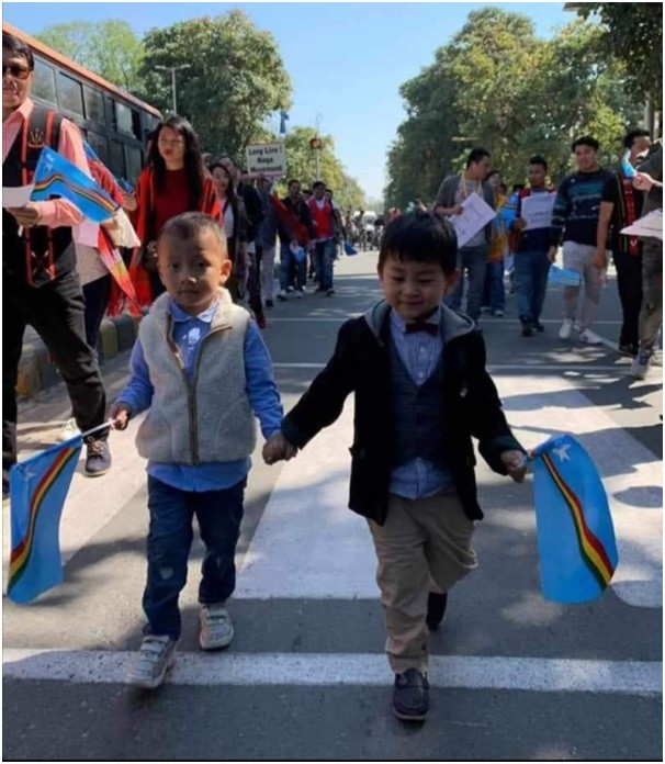 Two young Naga Heirs holding flags, symbolizing hope and unity during a peaceful political movement rally in New Delhi.