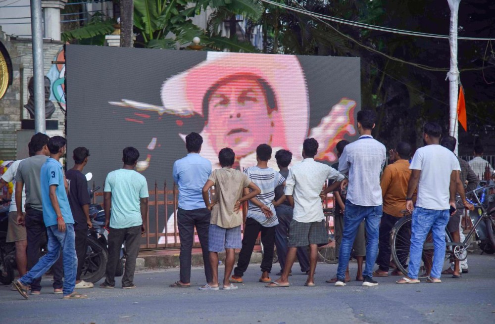 Nagaon: People look at a giant screen featuring singer Zubeen Garg on the roadside following his demise in Nagaon district of Assam on Sunday, September 21, 2025. (Photo: IANS)