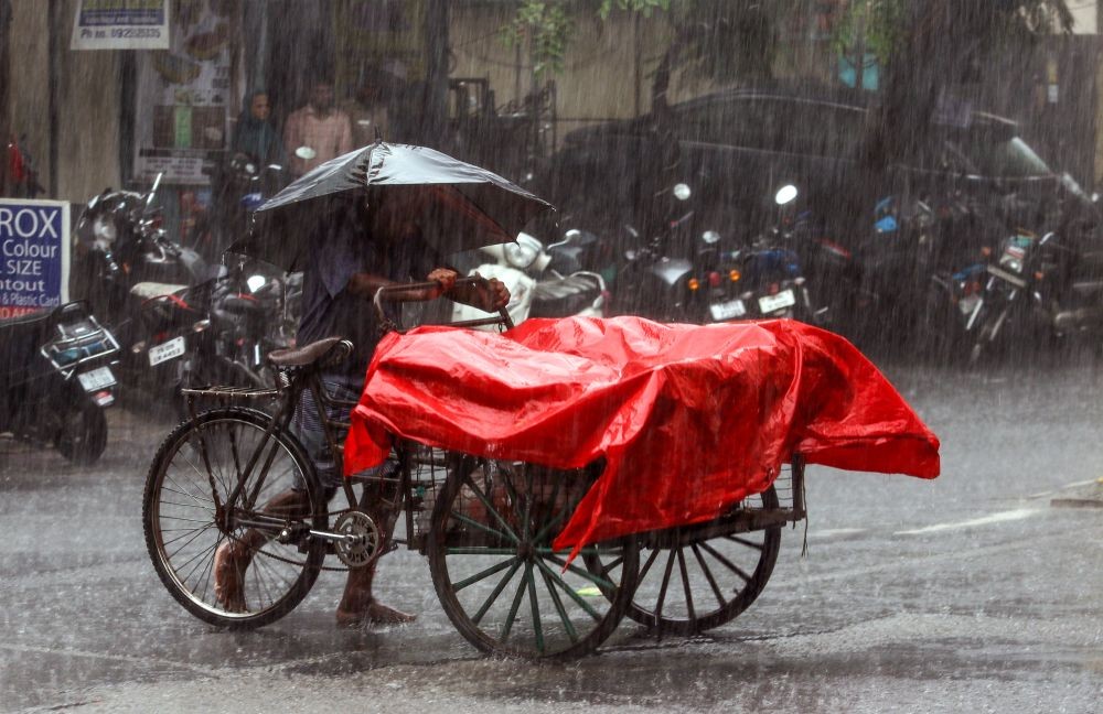 A cart vendor carrying an umbrella stands beside his cart covered with plastic sheets during heavy rainfall in Chennai on May 9, 2026. (IANS File Photo)